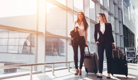 Two professional women walking through an airport terminal with luggage